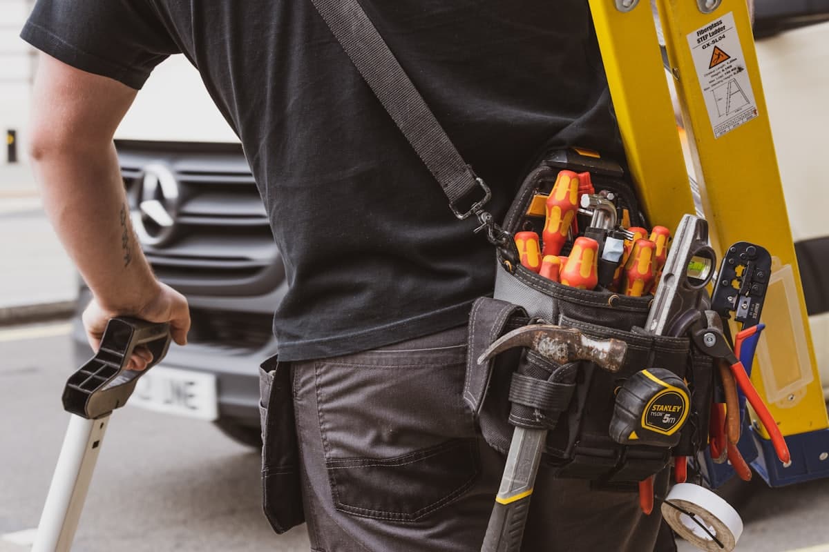 Tradesperson with a full tool belt carrying a ladder